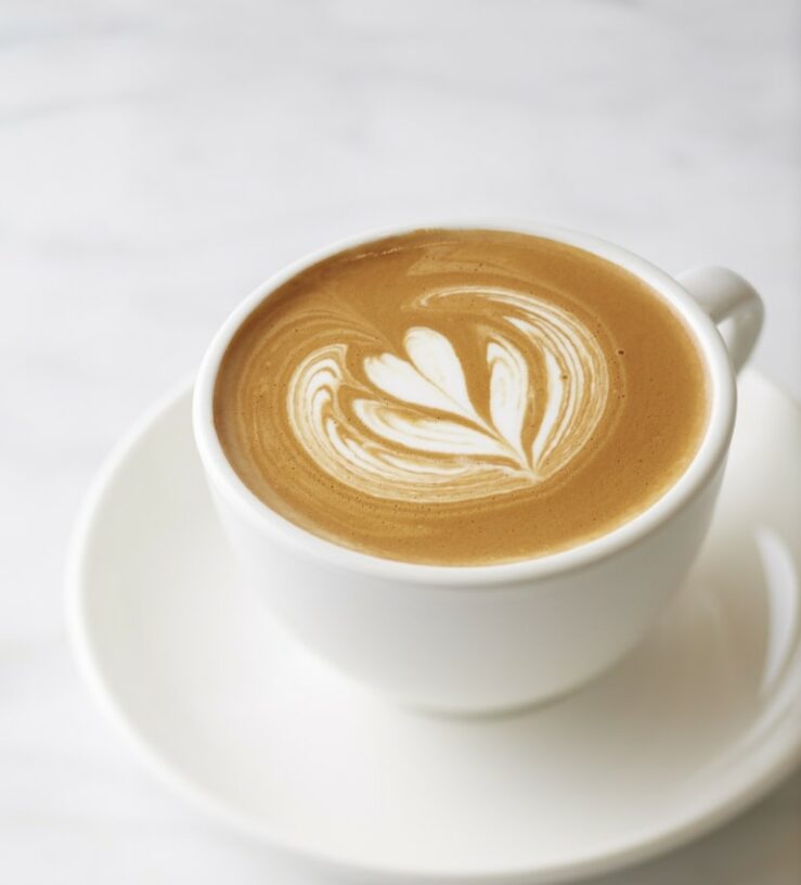 Photo of a coffee in a white mug on a white surface with a picture of a milky heart in the coffee