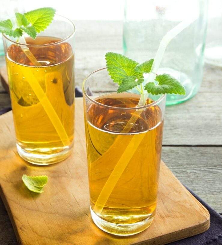 Two glasses of kombucha with mint and straws on a block of wood