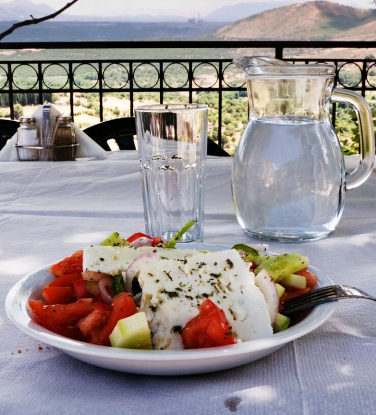 Photo outdoors on holiday of a greek salad with a jug and glass of water in the background