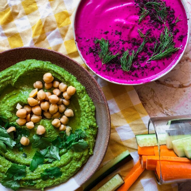 Photo of gut health friendly summer dips green hummus and beetroot dip on a table with vegetable sticks