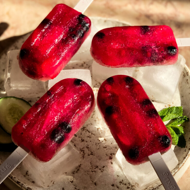 Four red fermented fizz ice lollies lying on ice cubes on a tray in the sunlight