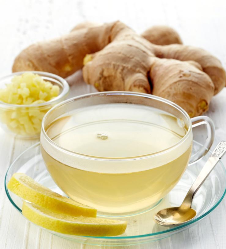 Photo of a glass of finger tea with ginger in the background and a slice of lemon on the side