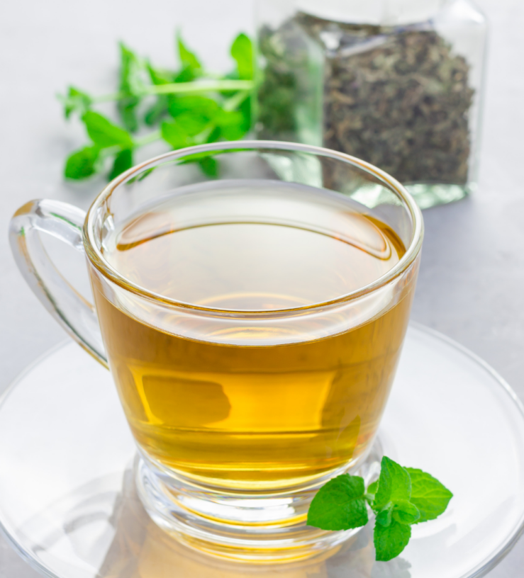 Glass of a peppermint tea on a table with peppermint leaves in the background