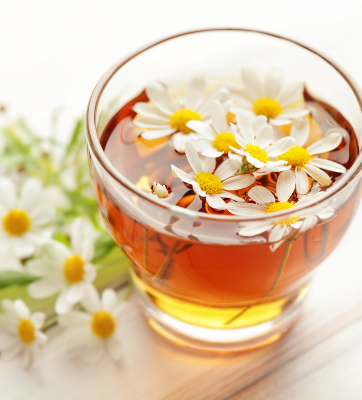 Photo of chamomile tea in a glass with flowers in the background