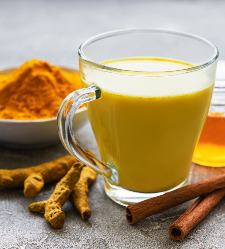 Photo of a glass or turmeric tea with spices in the background