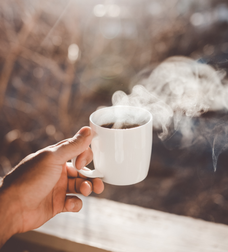 Photo of someone holding out a white mug of steaming tea