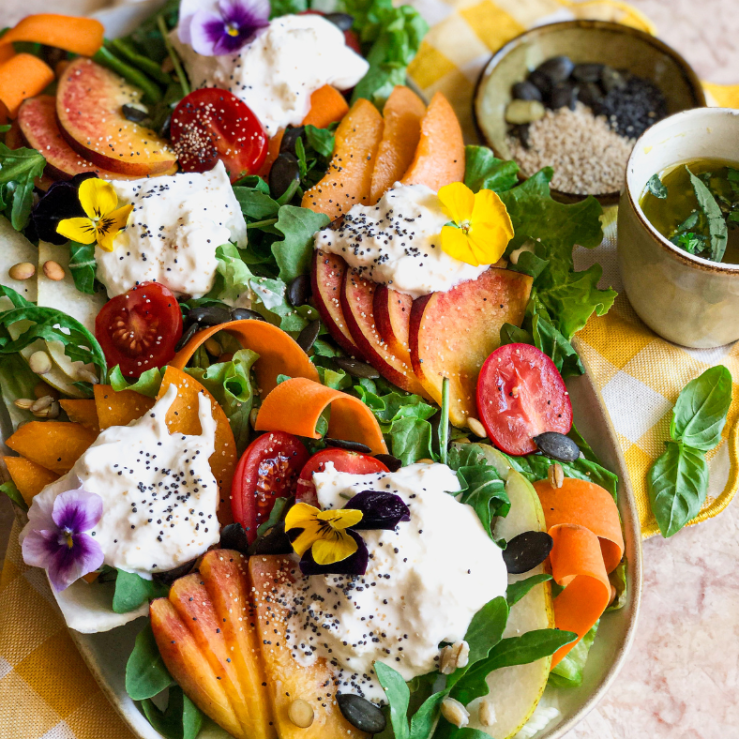 Photo of a vibrant end of summer salad including tomatoes, burrata, peaches, pears, seeds, rocket and other s