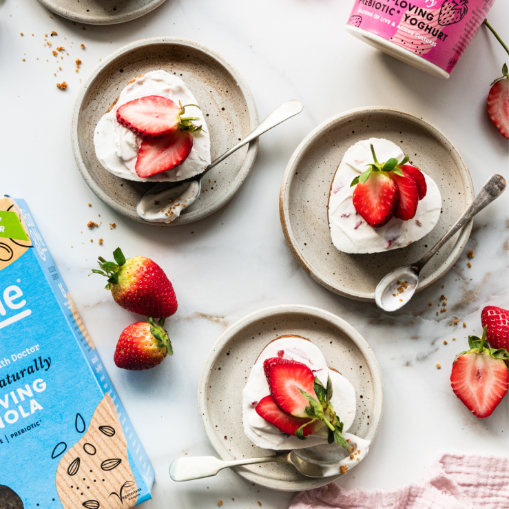 Photo of three small strawberry yoghurt pies on a white table with strawberries for decoration and packaging of Bio&Me in the background