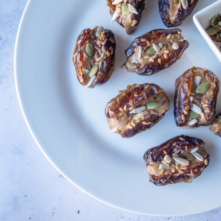 Plate spread with eight dates, stuffed full with nut butter and mixed seeds