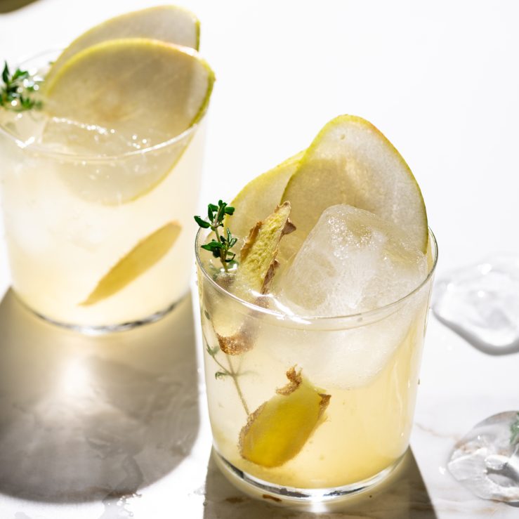 A glass of the pear & ginger spritz garnished with pear and thyme