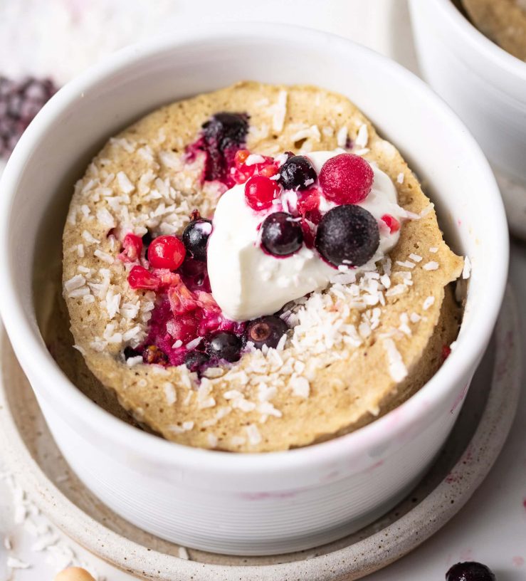 A photo of one of the mug cakes, in a white ramekin, topped with fresh berries and yoghurt