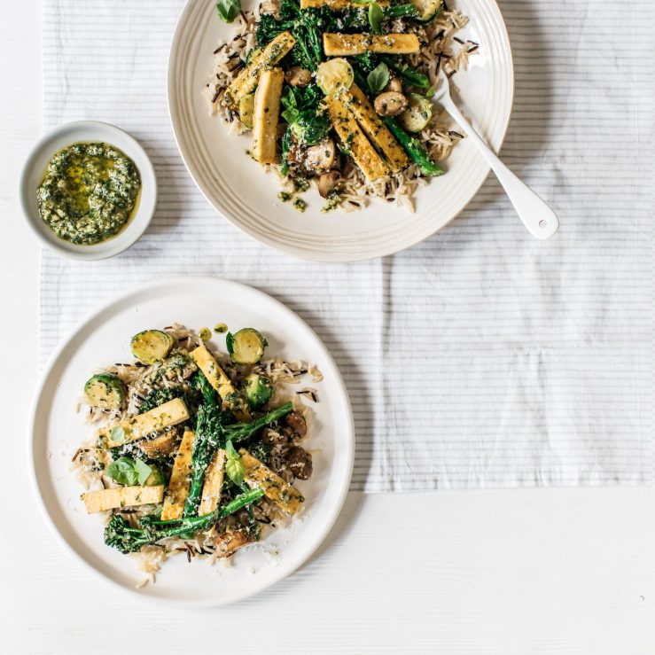 Two plates with Brussels sprouts & tenderstem broccoli & wild rice, served with a small pot of pesto between them