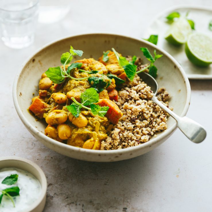 One bowl of cooked sweet potato and butter bean curry, with portion showing half grains and half curry. Served with a spoon