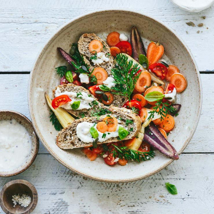 Ceramic bowl with quick carrot caesar salad, served with fresh brown bread slices and garnished with fresh mixed green herbs